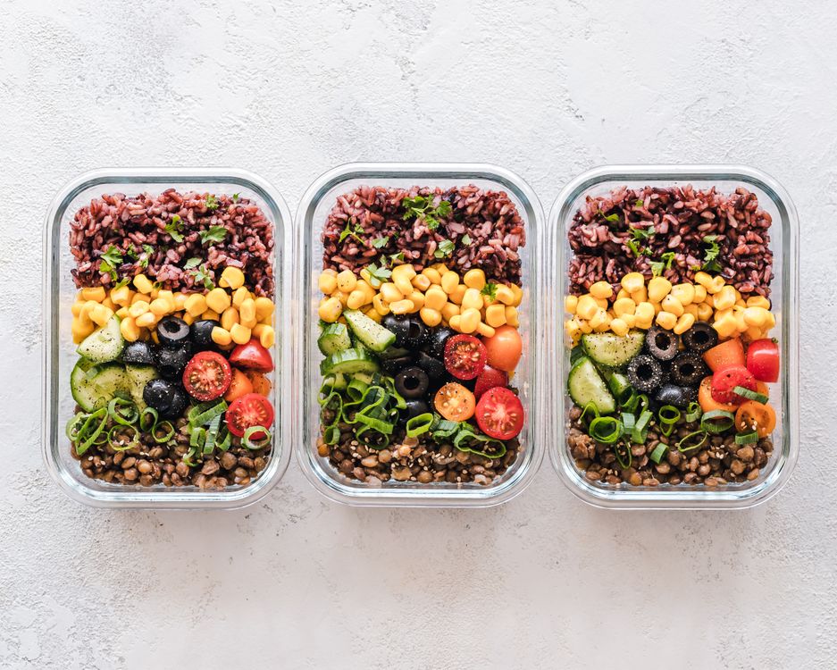 Glass meal prep containers filled with rice, corn, vegetables and lentils